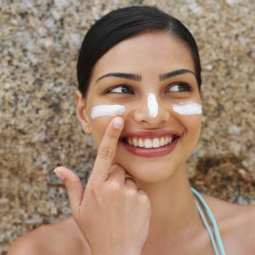 Woman happily applying sunscreen to her face to protect her skin while enjoying a day at the beach