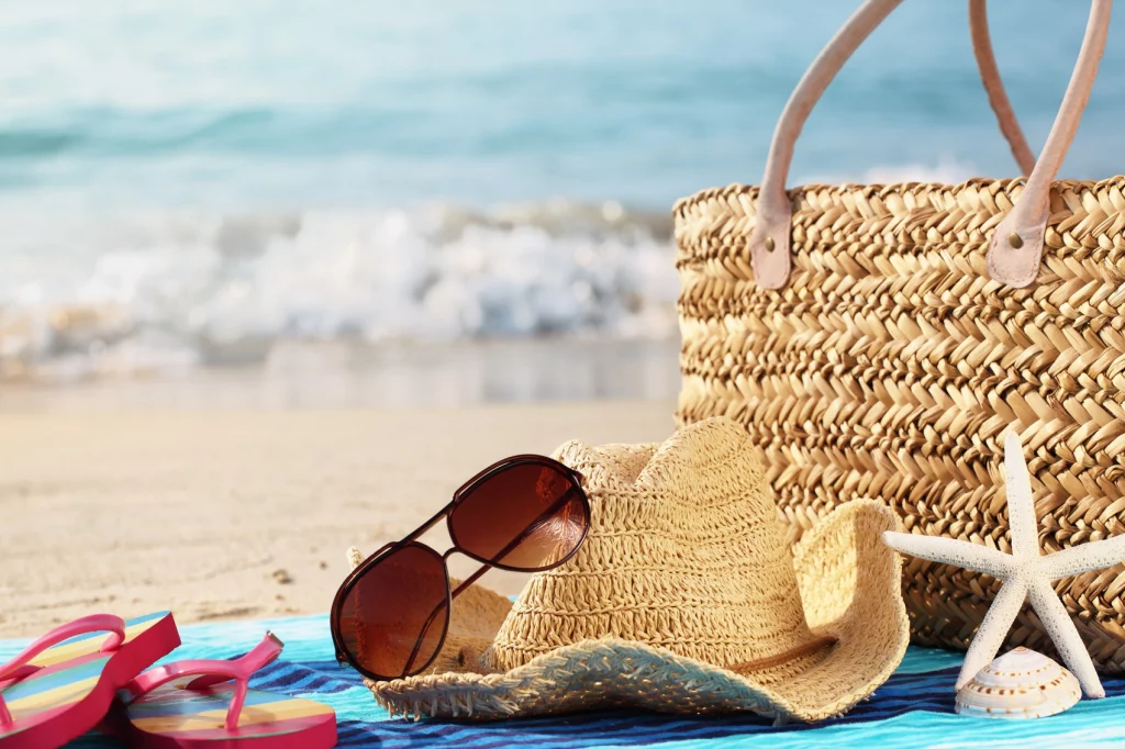 Women bag with sunglasses, flip flops, hat, and towel set up on the beach