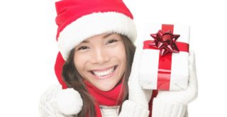 women in festive winter hat, sweater, and gloves holding a wrapped present and smiling