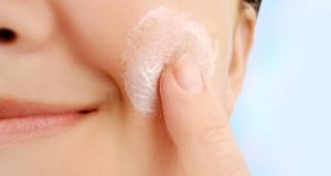 woman applying exfoliator to cheek