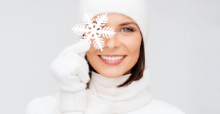 Woman in white sweater and hat holding decorative snowflake in front of eye