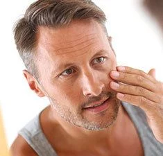 man checking reflection in mirror and considering Injectable Fillers