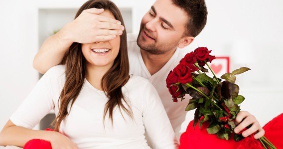 man covering woman's eyes to hide gift of bouquet of roses