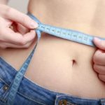 woman measuring her waistline with fabric measuring tape