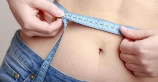 woman measuring her waistline with fabric measuring tape