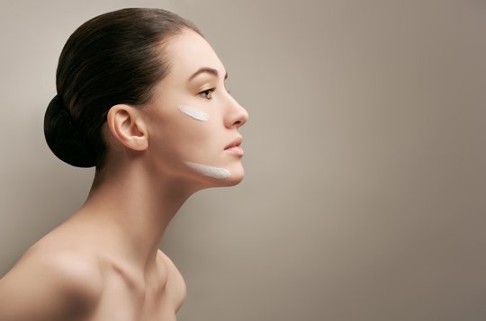 Brunette woman facing right with two cream stripes on her face.