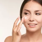 Brunette woman putting sunscreen on make up free face.