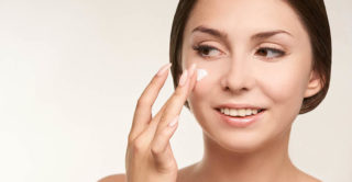 Brunette woman putting sunscreen on make up free face.