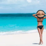 woman standing on sandy beach looking at blue ocean