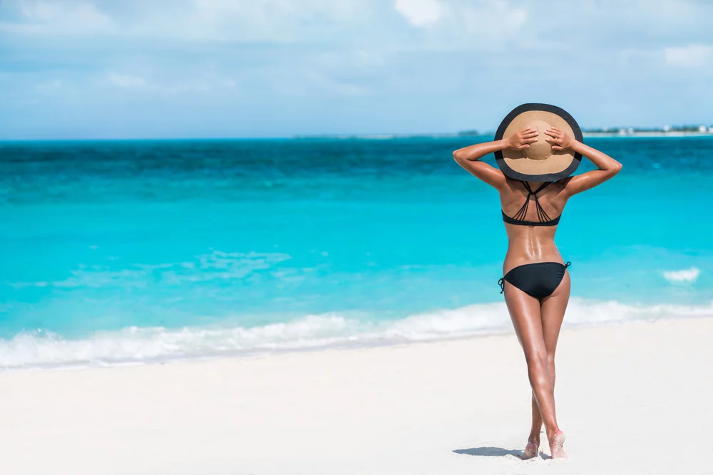 woman standing on sandy beach looking at blue ocean