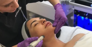 Esthetician using HydraFacial MD facial treatment on client's cheek