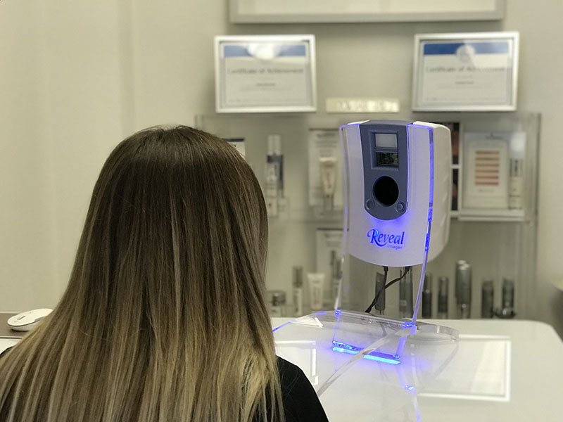 women in a medical room facing a Reveal Imager machine having her picture taken