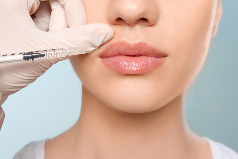 Close up of bottom half of young womens face as she gets lip injections from a doctor