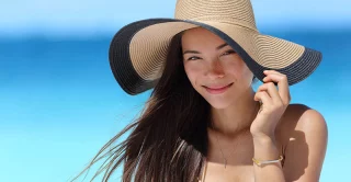 young women on beach wearing a big sun hat to protect her skin from sun damage