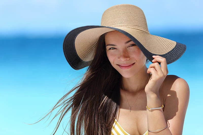 young women on beach wearing a big sun hat to protect her skin from sun damage