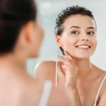 young women smiling and looking in the mirror with radiant flawless skin
