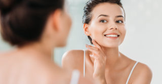 young women smiling and looking in the mirror with radiant flawless skin