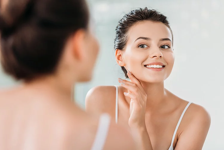 young women smiling and looking in the mirror with radiant flawless skin