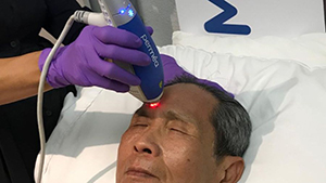 Esthetician using clear + brilliant treatment on client's forehead