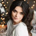 Close up portrait of a young beautiful smiling woman posing in an interior with festive Christmas lights on the background. Brunette model girl with a trendy makeup and perfect smooth skin.