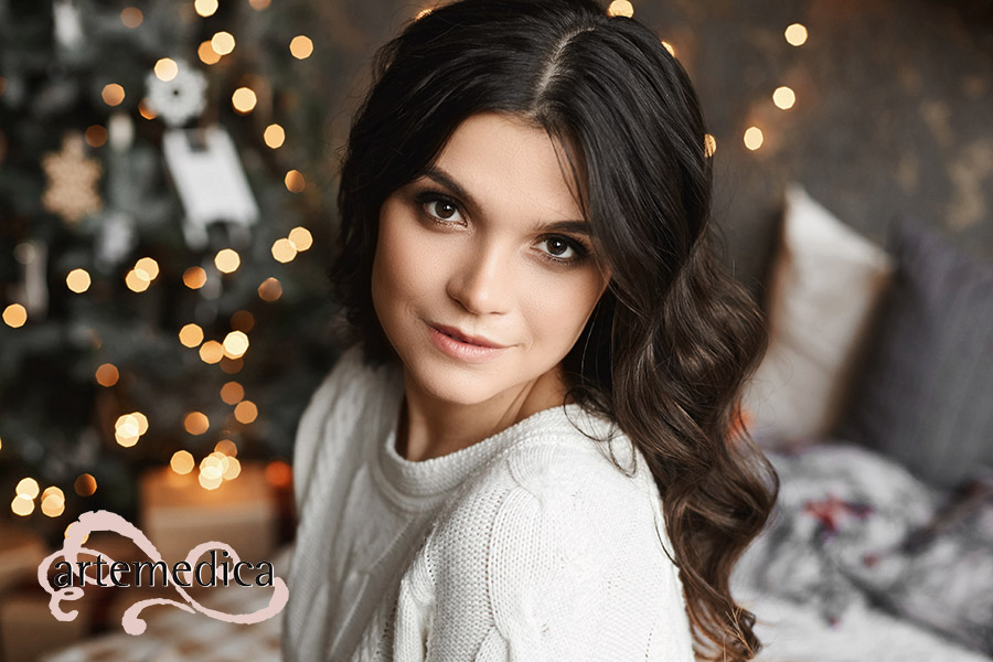Close up portrait of a young beautiful smiling woman posing in an interior with festive Christmas lights on the background. Brunette model girl with a trendy makeup and perfect smooth skin.