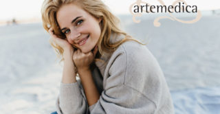 Portrait of charming young woman with blond hair, dressed in cashmere sweater. Girl sits on beach and enjoys fall day