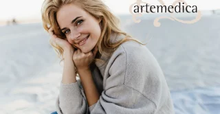 Portrait of charming young woman with blond hair, dressed in cashmere sweater. Girl sits on beach and enjoys fall day