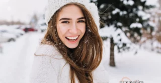 Woman with beautiful, youthful, glowing skin laughing while posing on snow background