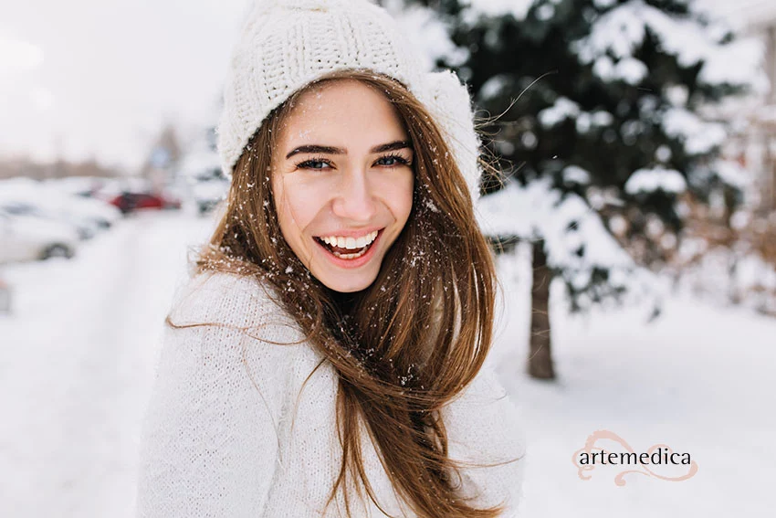 Woman with beautiful, youthful, glowing skin laughing while posing on snow background
