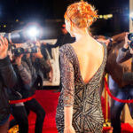 Celebrity walking down red carpet in beautiful black dress being photographed by paparazzi photographers