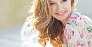 A beautiful women with long blonde hair and youthful, glowing skin, sitting outside on a sunny day wearing a floral dress