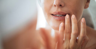 Middle-aged caucasian women looking closely into a mirror at her lips which look youthfully plump, hydrated, and wrinkle free