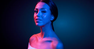 a beautiful women in blue and pink ambient lighting highlighting her tone and contoured facial featured from EmFace treatment