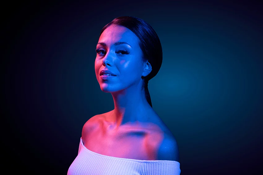 a beautiful women in blue and pink ambient lighting highlighting her tone and contoured facial featured from EmFace treatment