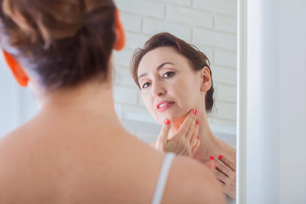 middle-aged woman looking in mirror and touching her chin