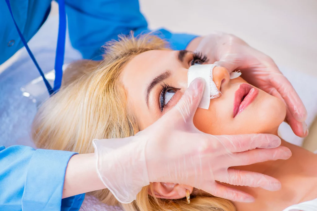 medical assistant applying a bandage to a woman's nose after successful rhinoplasty (nose surgery)