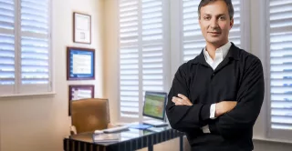 A smiling Dr. Victor Lacombe, wearing a black sweater, standing in his consultation room.