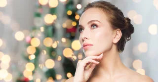 Bare-shouldered woman's head and shoulders, with hand under chin, Christmas tree background