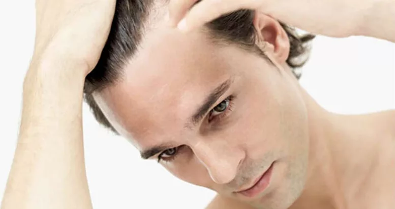 Young brown-haired man touching his receding hairline. 