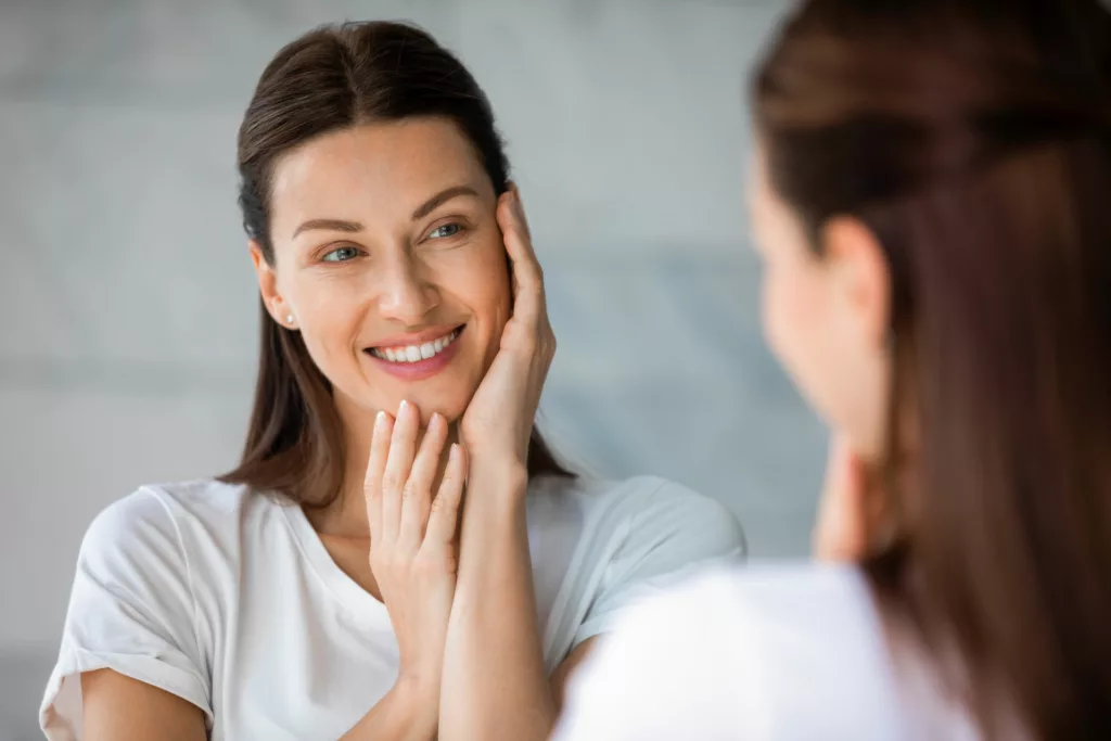 attractive young women admiring her appearance in the mirror and touching her cheeks with her hands