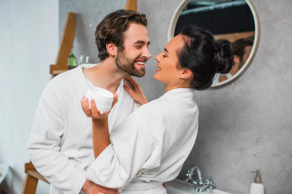 young man and his wife flirt in front of a mirror in their bathroom