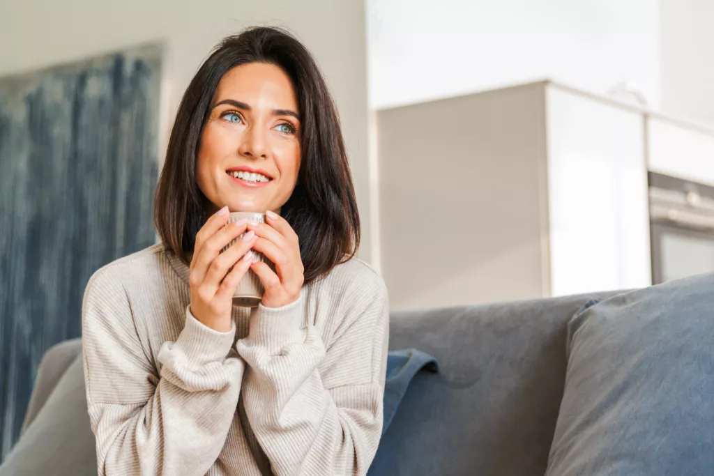 woman sitting on a sofa with a mug looking into the distance happily