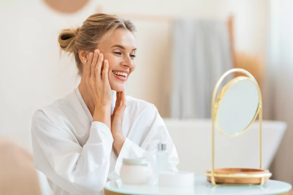 beautiful mature woman touching her face while admiring her cheekbones in a small mirror