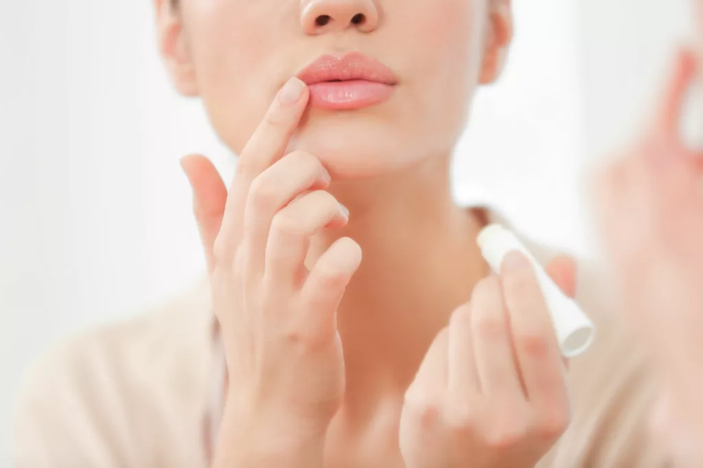 beautiful woman with full, plump lips applies lip balm in the mirror