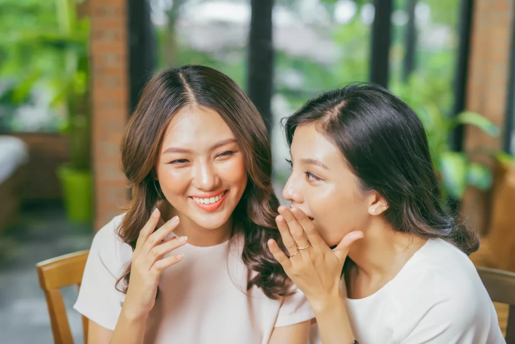 two lovely asian women smile, laugh and talk outside a quaint cafe