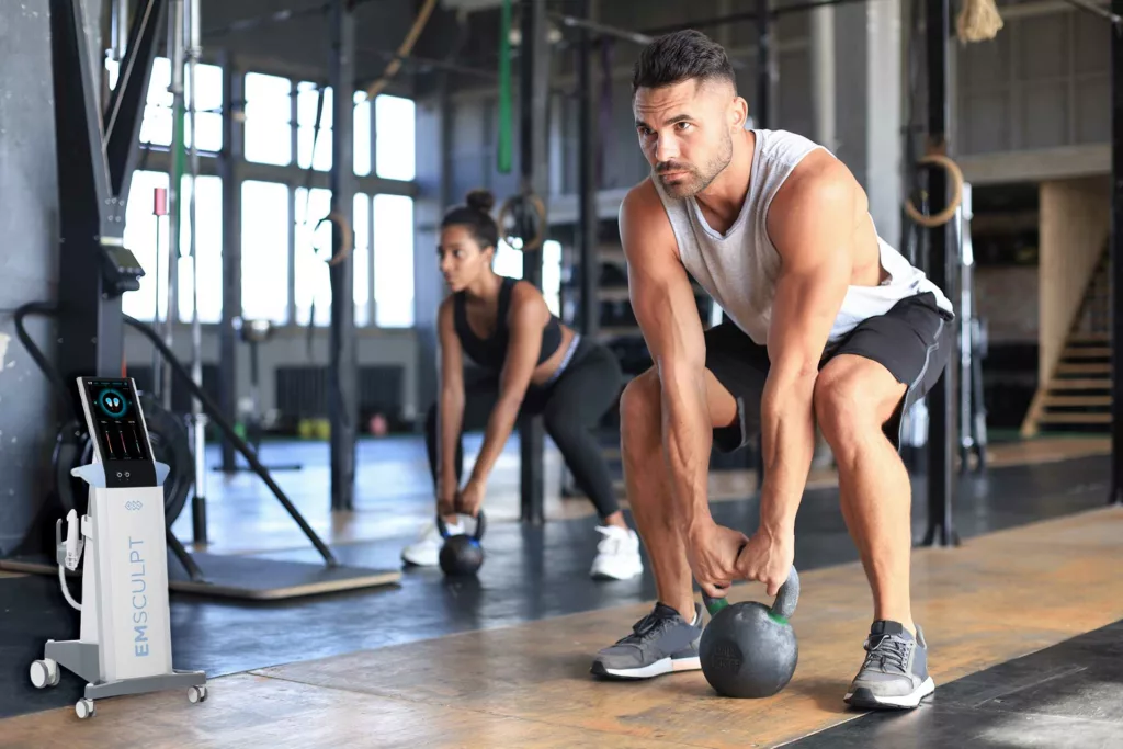 man and woman lift kettle bells together at a gym