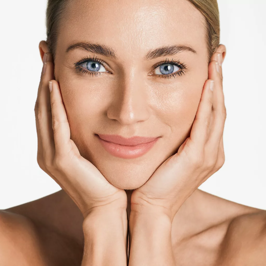 beautiful blonde-haired, blue-eyed woman cupping her cheeks and looking directly at the camera