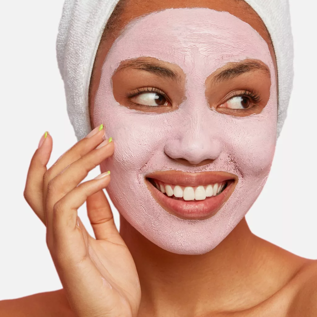 lovely African American woman has delicate sooth skin, wears cream mask on face