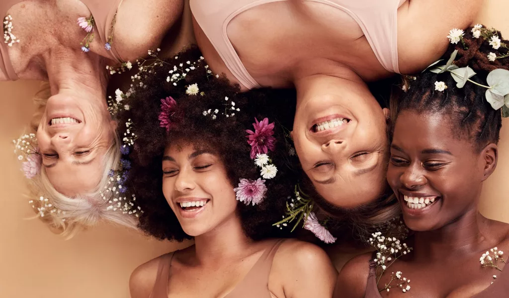 Women of different ages and skins tones laughing together with spring flowers in their hair.
