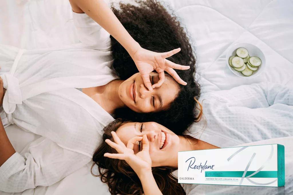 two young, beautiful hispanic women enjoying a spa day at home in robes and with cucumber masks